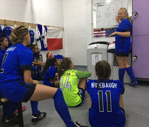 Girls in Blue Soccer Jerseys sitting in the locker room with purple lockers.