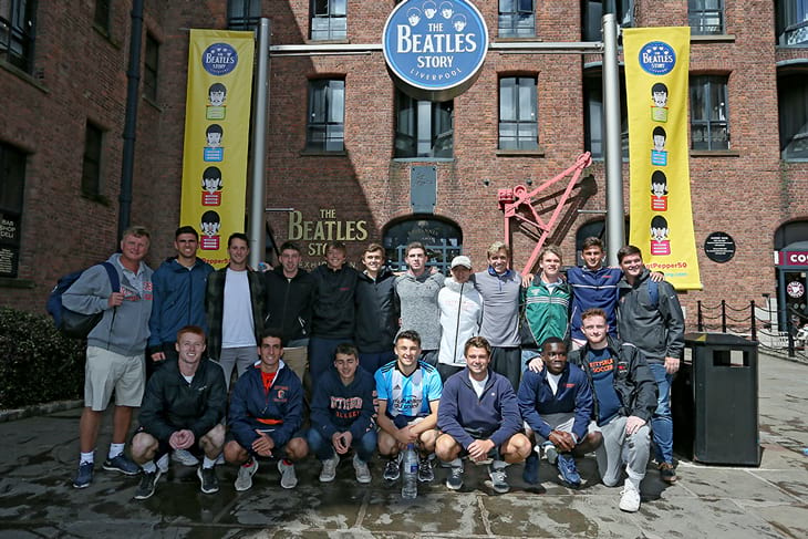 Two rows of soccer players standing and kneeling in front of a brick building dedicated to the Beatles.