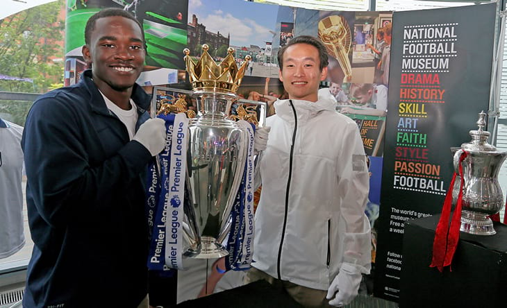 Two soccer players holding a large silver cup with blue ribbons.