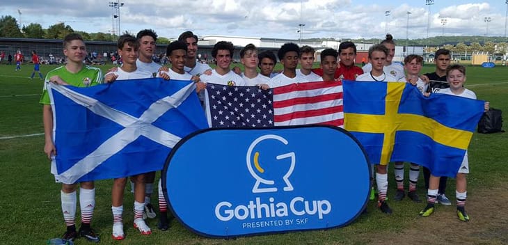 Soccer players from Maryland standing in front of three flags and a blue Gothia Cup sign.